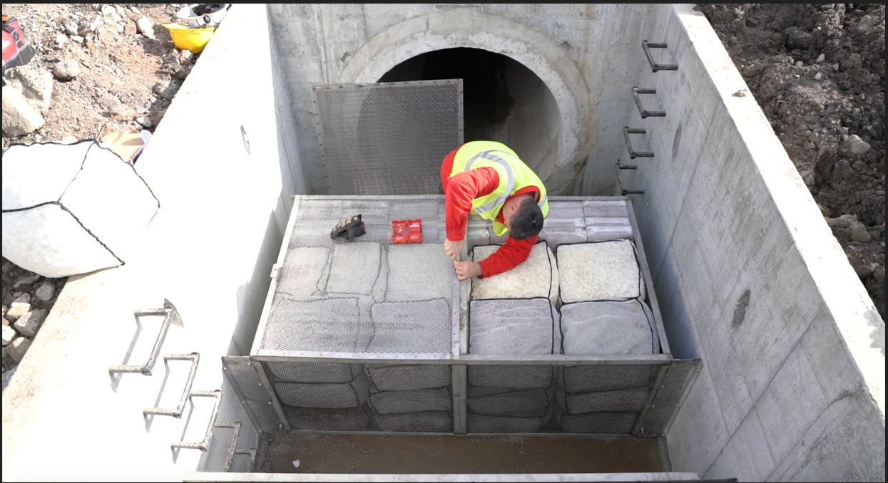 Technician in high-visibility gear installing Smart Sponge filtration media in a stormwater treatment system.
